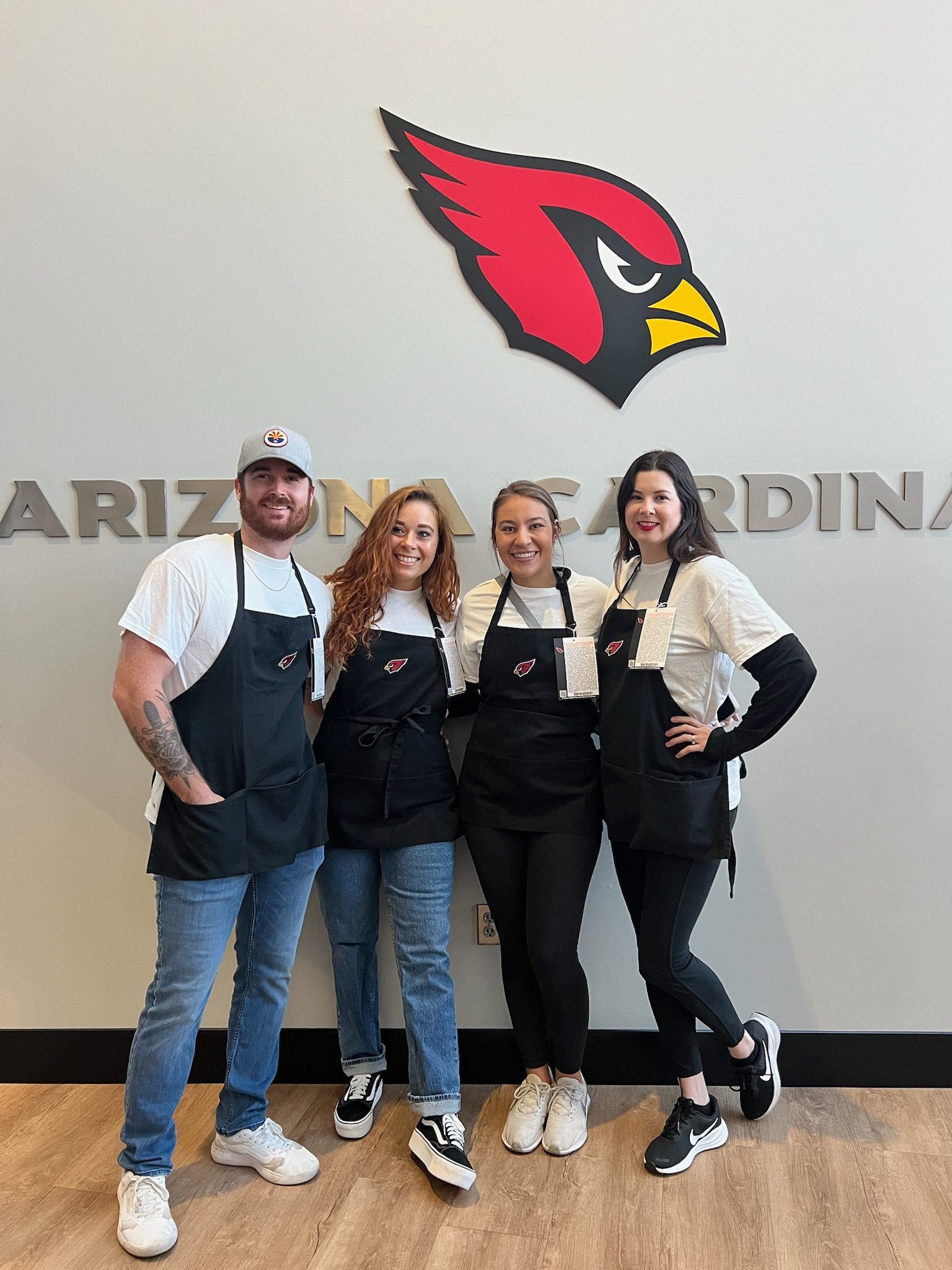 Four Young Professionals Board members in aprons in front of the Arizona Cardinals logo
